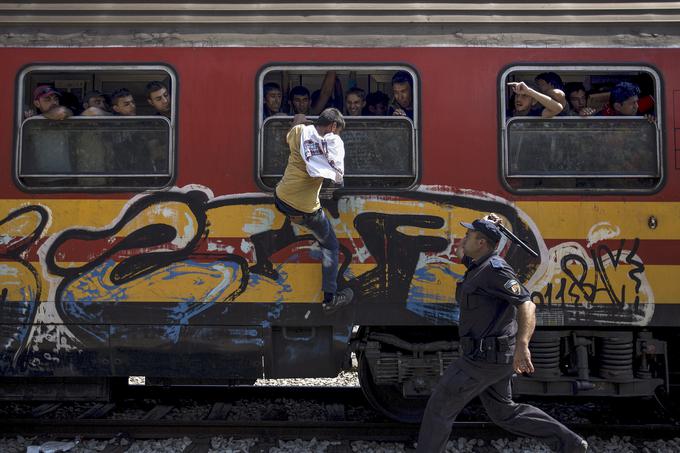 Policist želi migrantu preprečiti vkrcanje na vlak skozi okno na železniški postaji v makedonskem kraju Gevgelija blizu meje z Grčijo, 15. avgust 2015. | Foto: Reuters