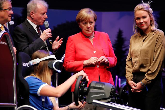 Nemška kanclerka opazuje dekle, ki igra simulator vožnje Gran Turismo.  | Foto: Reuters