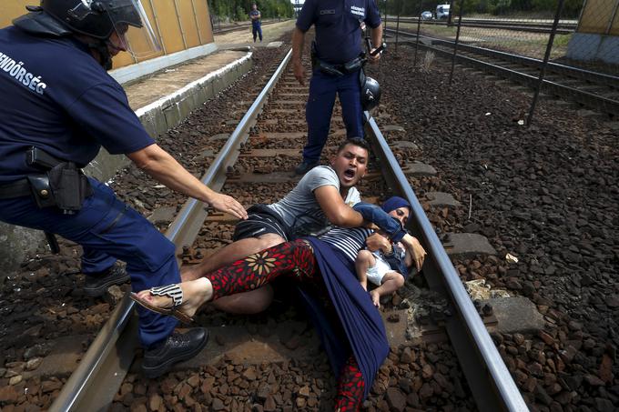 Madžarski policist sega proti migrantski družini, ki se je vrgla na progo, ker so jo hoteli zadržati na železniški postaji mesta Bicske na Madžarskem, 3. september 2015. | Foto: Reuters