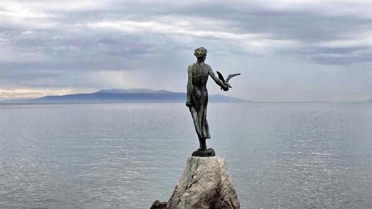 Dekle z galebom (Djevojka s galebom) je delo Zvonka Cara in stoji ob sprehajališču Lungomare od leta 1956. Zagotovo ena od najbolj fotografiranih opatijskih znamenitosti in simbol mesta je nadomestila kip Madonna del Mare, ki ga je leta 1893 ustvaril graški kipar Hans Rathausky kot spomenik tragične smrti avstrijskega aristokrata Arthurja Kesselstadta, njegove žene in njunega osebja v nevihti na morju pred Opatijo pred veliko nočjo leta 1891 (ta kip je najedel zob časa in so ga po prenovi postavili v Vilo Angiolina, pozlačena replika pa stoji pred cerkvijo svetega Jakova). Dekle z galebom upodablja morje, lepoto obale in pomorski pozdrav morju, avtor pa je dolgih pet desetletij skrival, po komu je upodobil dekle. Šele pred dobrim desetletjem so potrdili, da je šlo za avtorjevo sosedo iz Crikvenice Jeleno Jendrašić, ki je pozirala za uslugo prijatelju in ni zahtevala nobenega nadomestila. | Foto: Srdjan Cvjetović