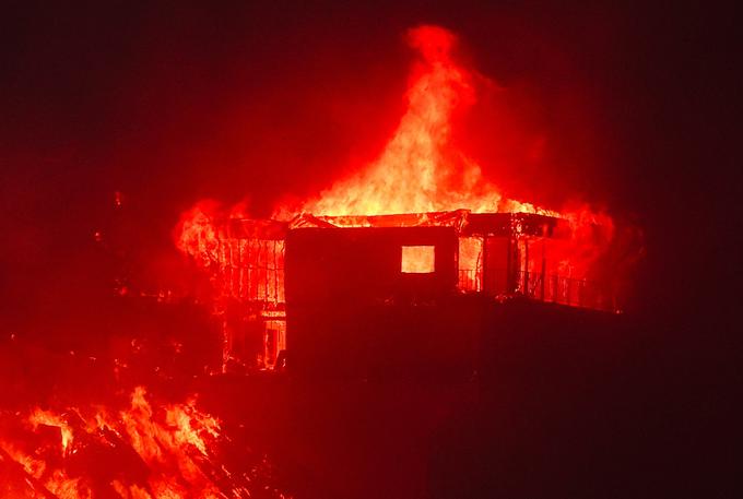 Plameni se dvigajo iz hiše ob obali ob cesti v Malibu. | Foto: Reuters