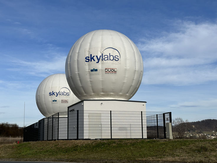 Sateliti v vesolju opravljajo zelo konkretne naloge – na primer opazujejo Zemljo, spremljajo okoljske spremembe, omogočajo komunikacijo ali zbirajo podatke za znanost in varnost. SkyLabs razvija ključne elektronske sisteme, ki satelitu omogočajo, da vse to sploh lahko počne. To so njegovi "možgani", ki skrbijo za delovanje, sistemi za komunikacijo z Zemljo in sistemi za upravljanje energije. Poenostavljeno: njihovi izdelki satelitu omogočajo, da ve, kaj počne, da lahko pošilja podatke nazaj na Zemljo in da zanesljivo deluje v zelo zahtevnih pogojih vesolja. Brez teh sistemov satelit ne more delovati, podobno kot telo ne more delovati brez živčnega sistema oz. organov. 
Na fotografiji je zemeljska postaja SkyLabs v Zrkovcih pri Mariboru, preko katere komunicirajo s sateliti v vesolju.  | Foto: arhiv podjetja