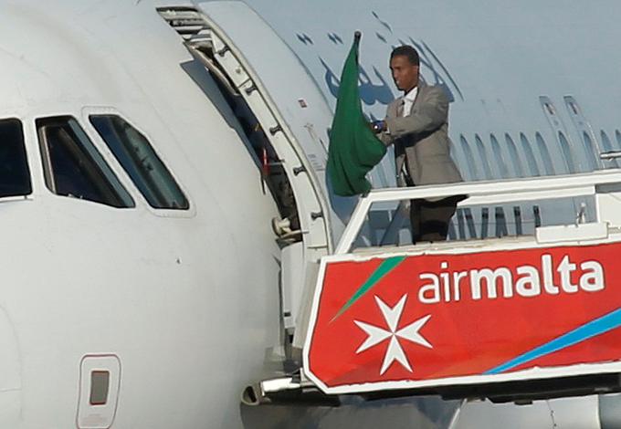 Ugrabitelj je na vratih letala v rokah držal staro libijsko zastavo, ki so jo uporabljali v Gadafijevem času. | Foto: Reuters