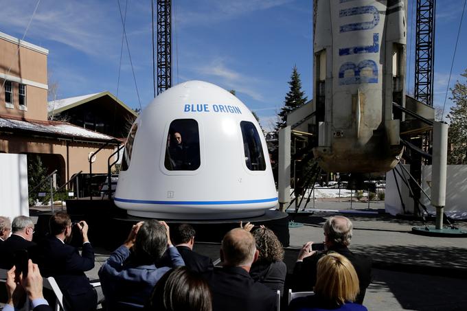 Jeff Bezos kuka iz makete potniške kapsule podjetja Blue Origin, ki bi v vesolje že naslednje leto lahko odpeljala prve turiste. V ozadju je velikanska raketa New Shepard, ki je, to izdaja tudi njena zdelana zunanjost, naš planet že nekajkrat videla "od zgoraj". Prav New Shepard bo tisti, ki bo vesoljske turiste odpeljal v nizko Zemljino orbito. Podjetje Blue Origin je po uspešnosti poletov v vesolje in navpičnih pristankov na Zemlji po mnenju večine strokovnjakov sicer vsaj tako uspešno kot SpaceX, ki ga vodi Elon Musk. | Foto: Reuters