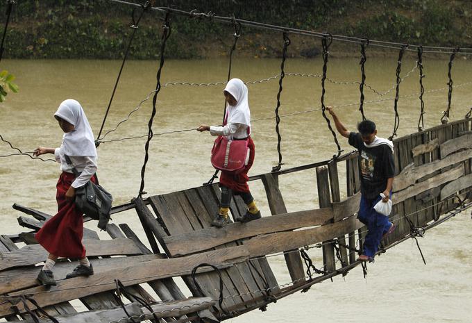 Otroci se držijo jeklenih palic zrušenega mostu med prečkanjem reke. Indonezija, regija Lebak. | Foto: Reuters