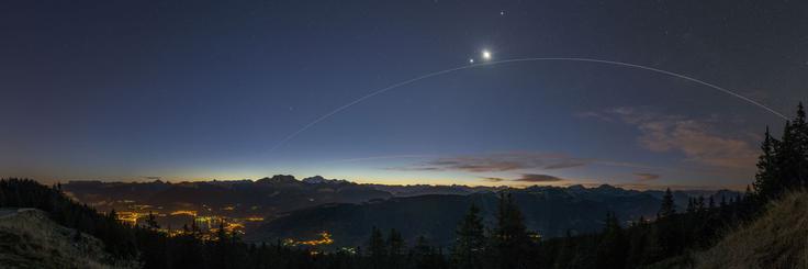 Lok svetlobe, ki ga je med potjo okrog Zemlje nad francoskim mestom Annecy za sabo pustila Mednarodna vesoljska postaja (ISS). Visoko na nebu tesno skupaj sijeta Luna in planet Venera. Foto: Scott Carnie Bronca. | Foto: 