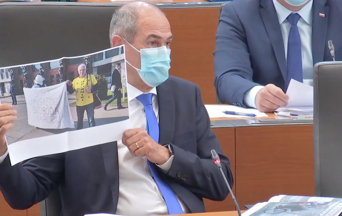 Janša | Janez Janša v državnem zboru kaže fotografijo, na kateri je protestnik Igor Bricelj pred stavbo DZ s transparentom Smrt janšizmu, svoboda narodu. | Foto zajem zaslona