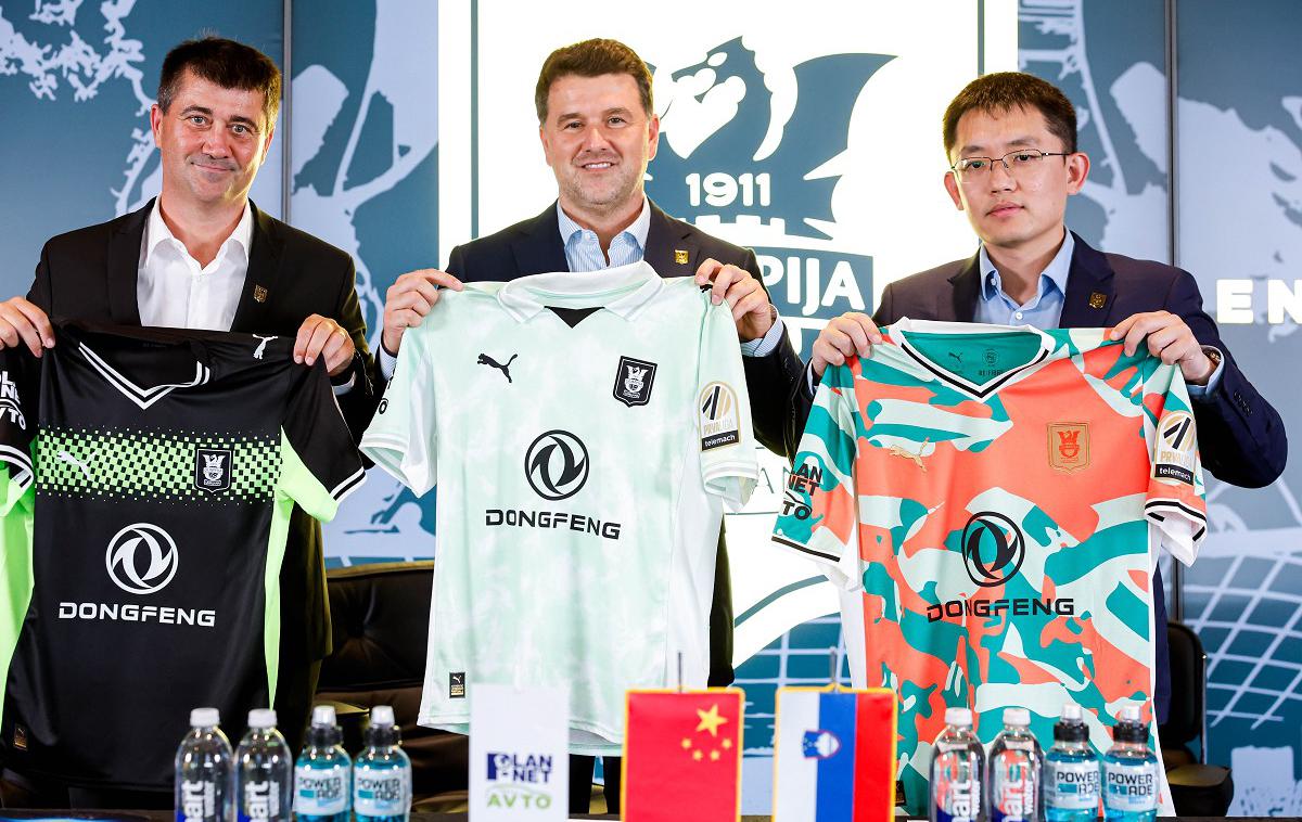 NK Olimpija | Direktor Olimpije Igor Barišić, direktor podjetja Plan Net Avto Marko Femc in Xie Qian, vodja evropskega predstavništva Dongfeng, so predstavili tekmovalne drese Olimpije za sezono 2025/26. | Foto Aleš Fevžer
