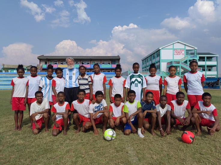 Pedro Opeka v družbi mladih nogometašev in nogometašis z Madagaskarja. Ena od njih nosi dres Zlatka Zahovića, medtem ko je Opeka v argentinskem dresu legendarnega Maradone.  | Foto: osebni arhiv Anje Kovačič