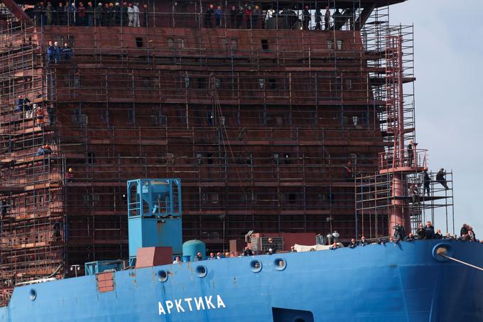 Gradbeni delavci na bližnji ladji, natančneje ledolomilcu Arktika, ki ga poganja jedrski reaktor, opazujejo odhod plavajoče jedrske elektrarne iz pristanišča v Sankt Petersburgu. | Foto: Reuters