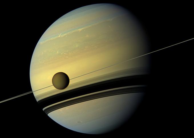 Saturn se lahko tolaži s tem, da je njegova luna Titan (v ospredju) edina z gosto atmosfero in površinskimi tekočimi (ni vode, temveč utekočinjeni ogljikovodiki, na primer metan) telesi. Klikni na fotografijo za zgodbo o Titanu. | Foto: Reuters