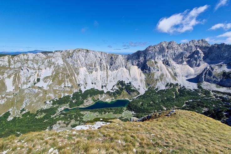 Tik pod vrhom se odpre vrhunski pogled navzdol na Veliko Škrčko jezero. Na drugi strani (desno) je tako imenovana Soa Nebeska – najvišji vrhovi Durmitorja: Bezimeni vrh, Bobotov kuk in Đevojka. | Foto: Matej Podgoršek