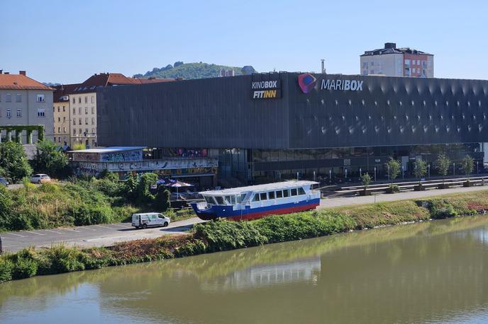 Ladijca v Mariboru | Pred kratkim so okoli 22 metrov dolgo in skoraj 40 ton težko ladjo na nabrežju, poleg katerega leži občinsko parkirišče, prebarvali na belo, modro in rdečo.  | Foto STA